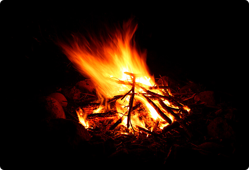 Flames of a cozy campfire flicker in a light breeze against a dark night.