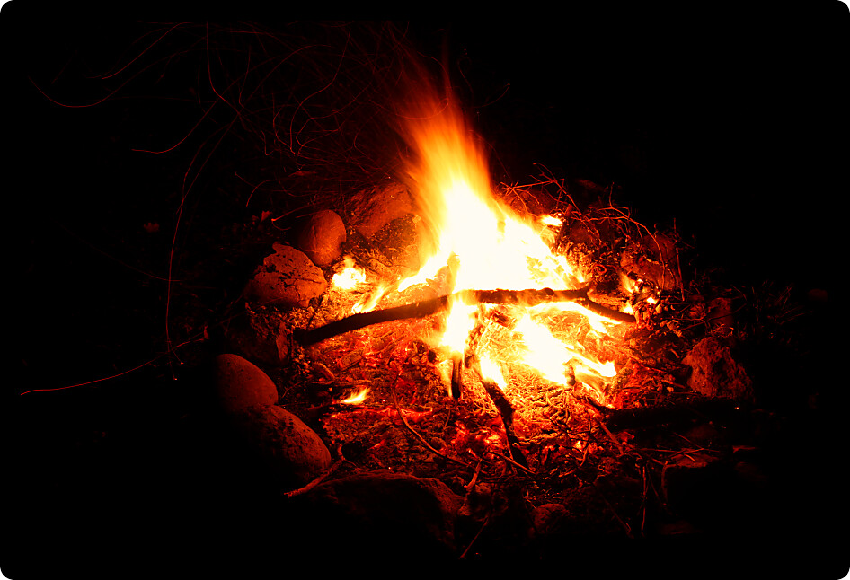 Flames of a cozy campfire flicker in a light breeze against a dark night.