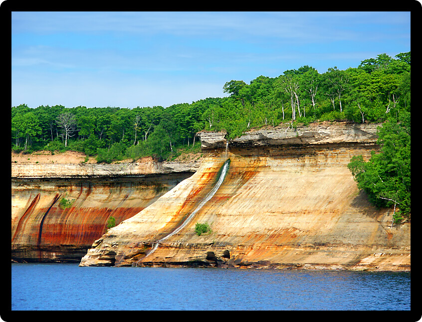 Bridalveil Falls flows down a steep rocky shoreline into Lake Superior at Pictured Rocks National Lakeshore Michigan.