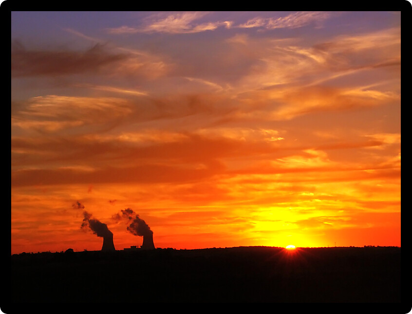 Vivid colors in the sky as the sun sets over two giant cooling towers at a nuclear plant.
