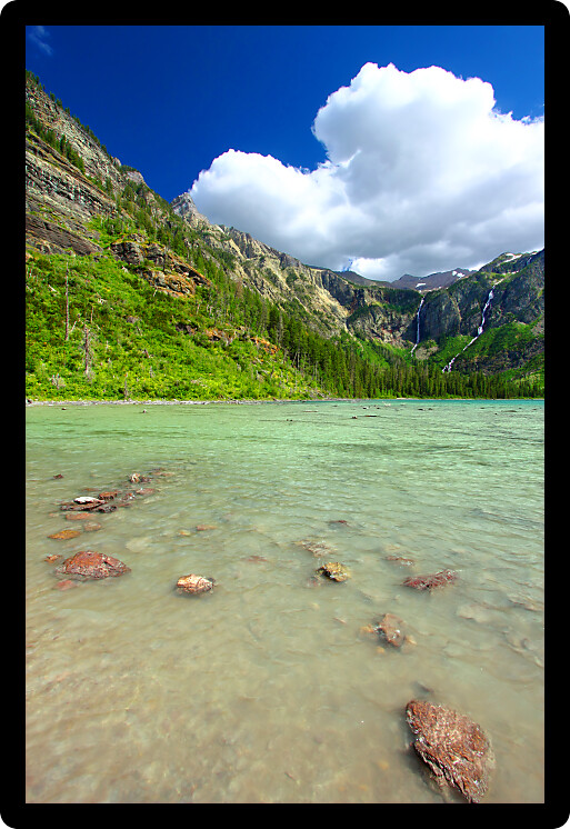 Puffy clouds cruise through the skies above Avalanche Lake in Glacier National Park of Montana.